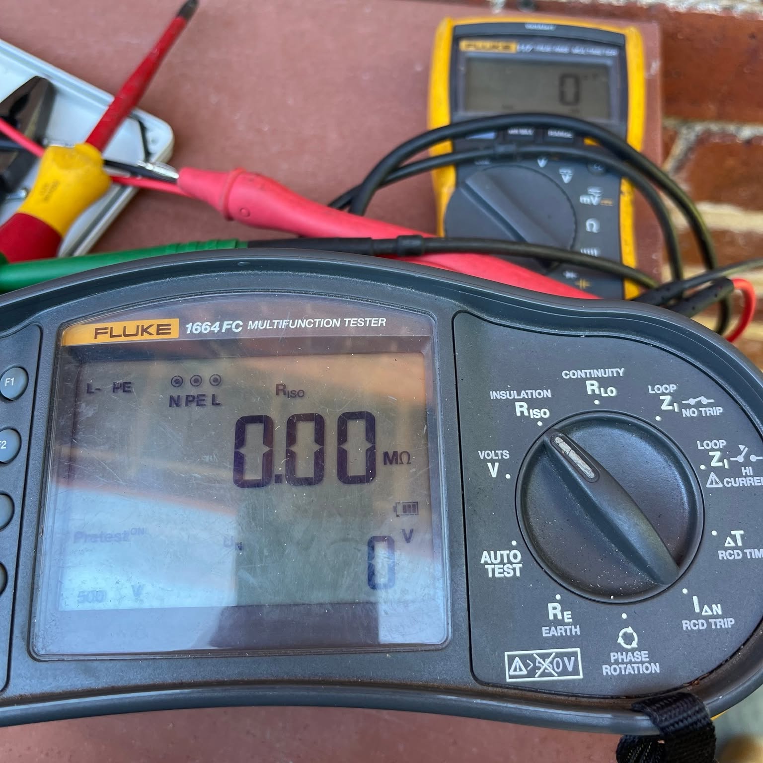 Fluke 1664 FC multifunction tester and a Fluke multimeter on a brick step